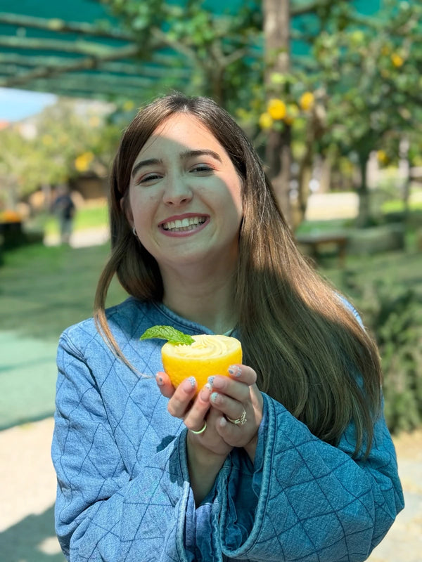 Smiling woman holding a lemon in a lemon grove during a gluten free cooking class.