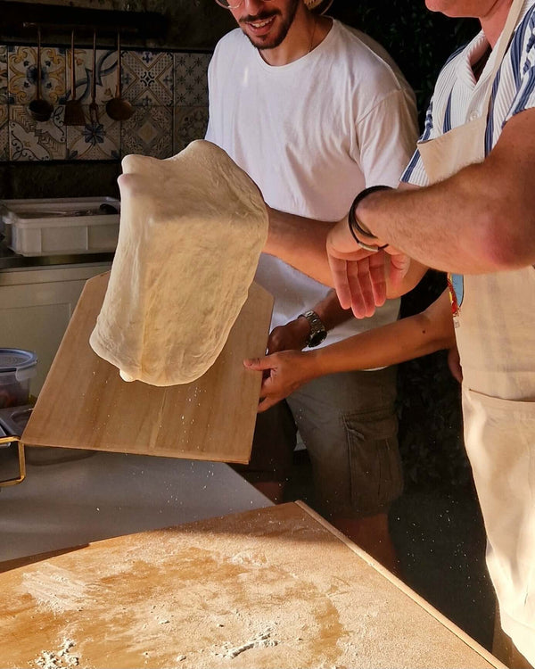 Participants in a Pizza Making Class skillfully tossing pizza dough in a seaside lemon grove.