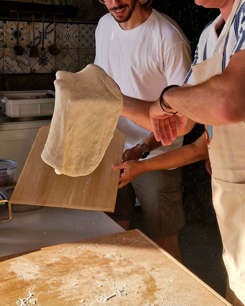 Participants in a Pizza Making Class skillfully tossing pizza dough in a seaside lemon grove.