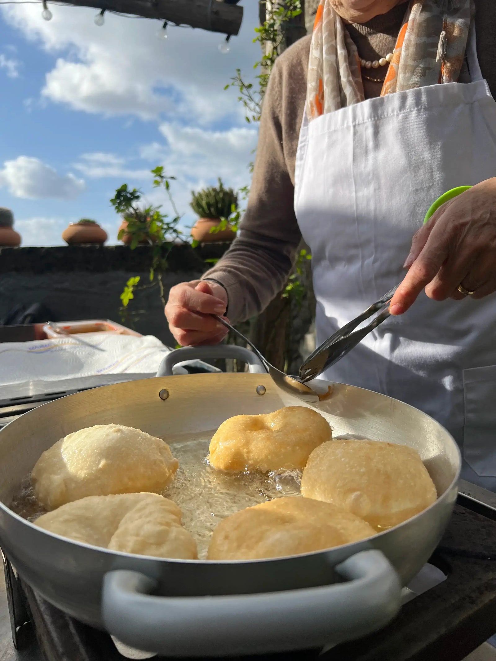 A participant in a Pizza Making Class frying dough in a pan under a sunny sky in a lemon grove.