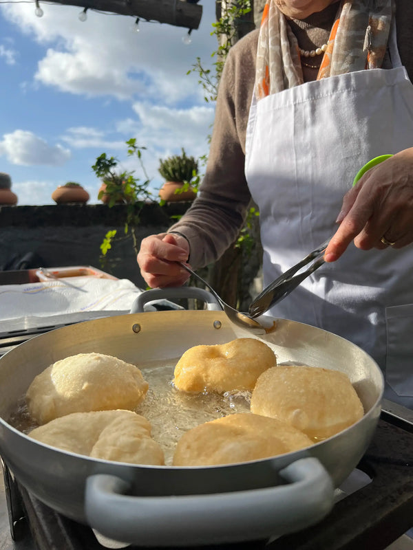 A participant in a Pizza Making Class frying dough in a pan under a sunny sky in a lemon grove.