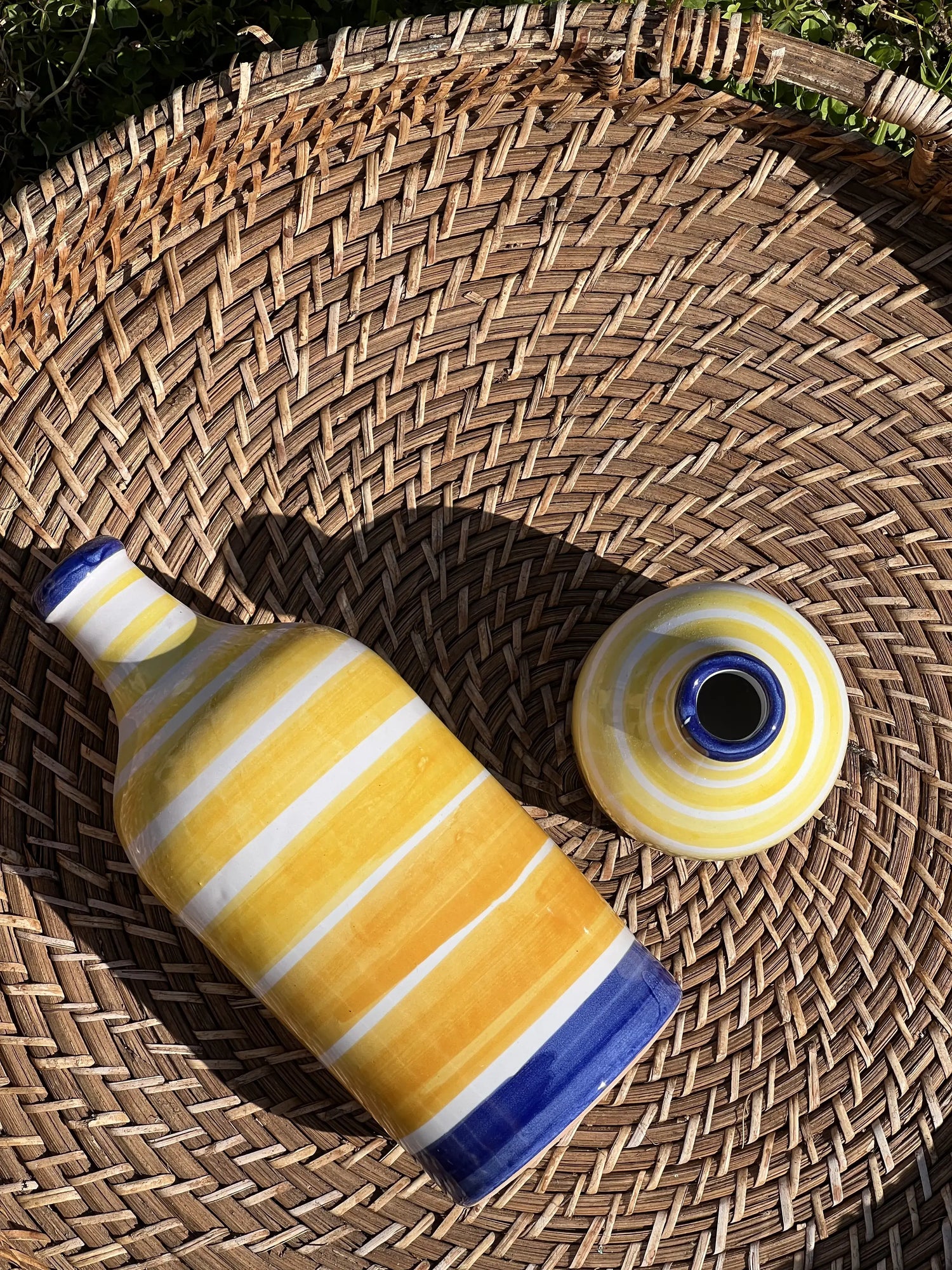 Yellow and blue ceramic Limoncello bottle on woven basket, part of Limoncello Kit Sorrento with IGP Sorrento Lemons.