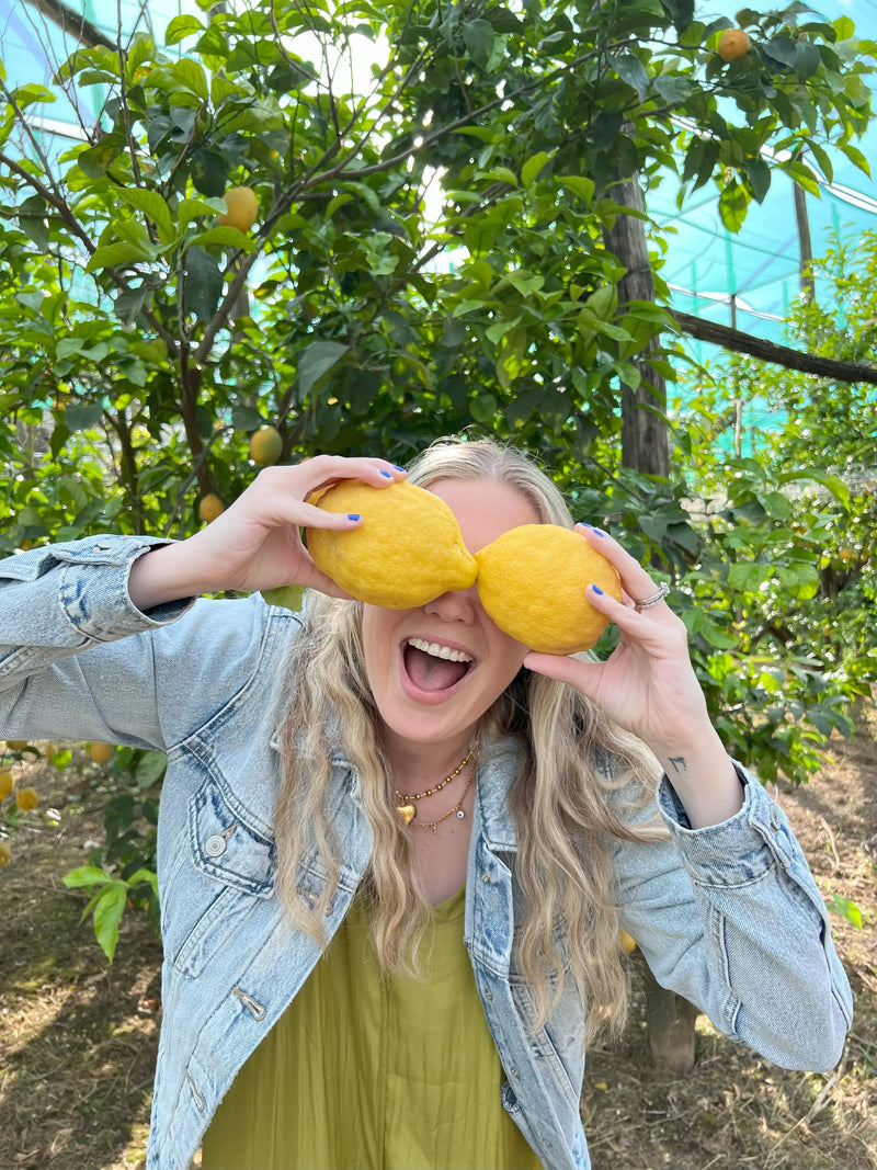 Limoncello tour participant holding lemons in front of her face in a lemon grove.