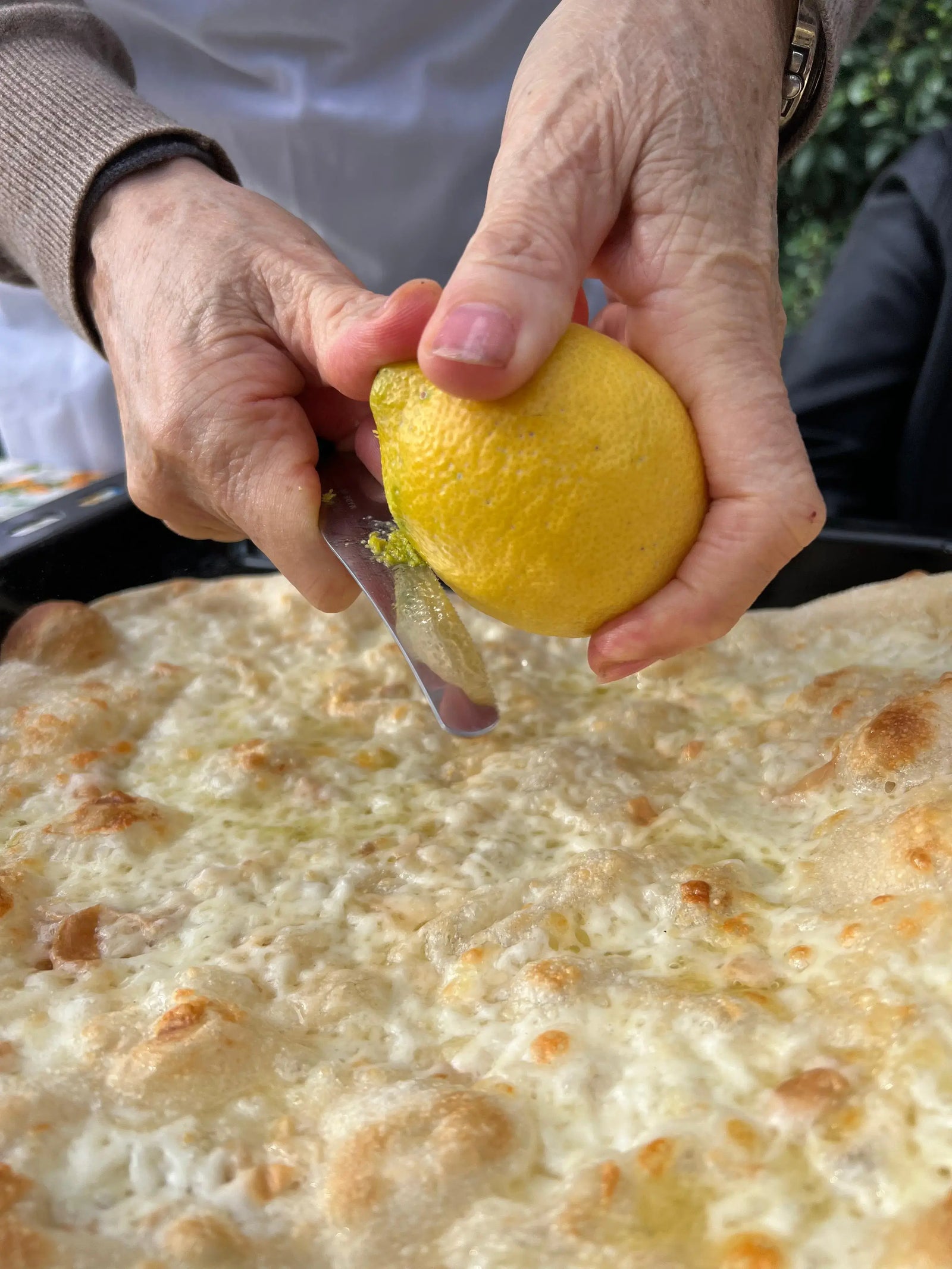 Hands squeezing a lemon over a freshly made pizza during a private pizza making class.