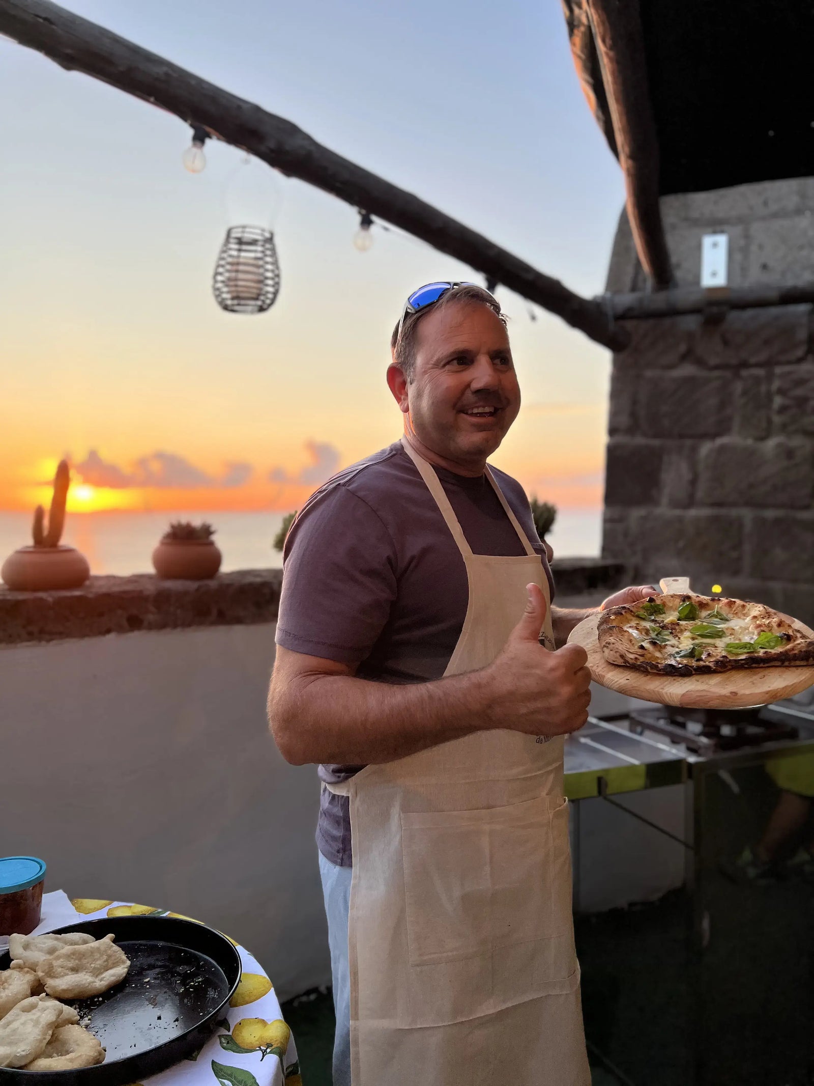 Man enjoying a Pizza Making Class in a seaside lemon grove, showcasing a freshly made pizza at sunset.