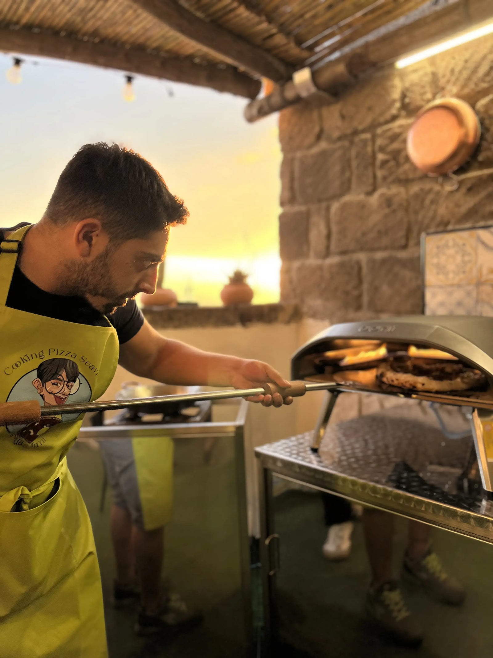 Man in an apron retrieving freshly baked pizza in a private pizza making class with sea view.