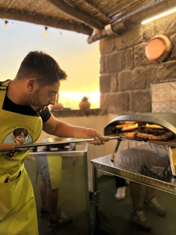 Man in an apron retrieving freshly baked pizza in a private pizza making class with sea view.